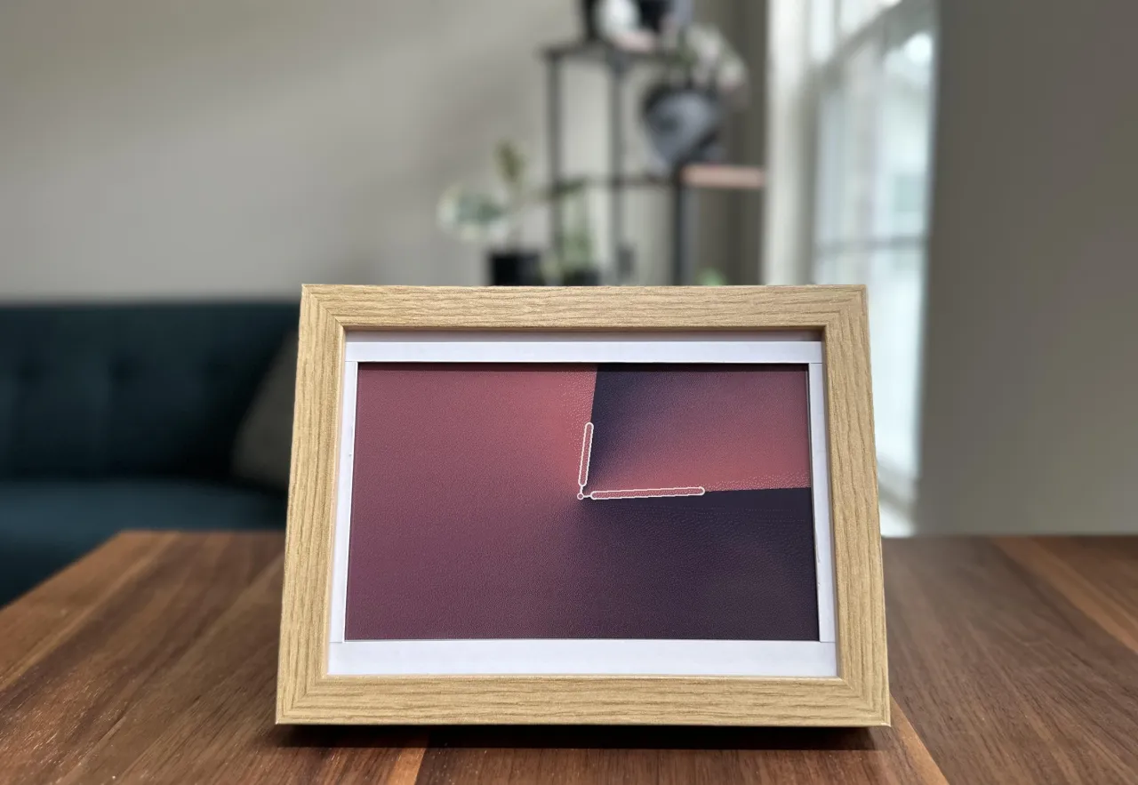 InkyPi e-ink display in a wooden picture frame showing a clock face